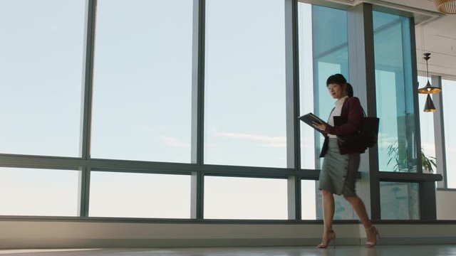 asian business woman using tablet computer walking through office sending email messages successful female executive browsing on mobile device leaving workplace