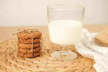 A stack of cookies and a glass of milk stand on a wooden napkin on the table.