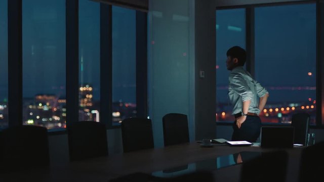 asian businessman working late using laptop computer in office project manager brainstorming ideas for company looking out window at city thinking of deadline