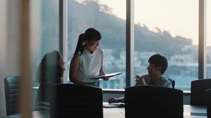 business people working late asian team leader woman meeting with colleagues discussing project manager sharing ideas on tablet computer group of executives brainstorming in office at sunset - Powered by Adobe