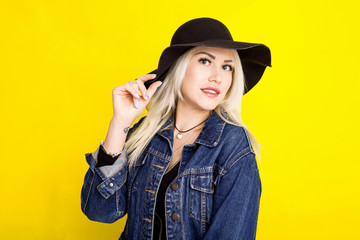 beautiful blonde girl in a hat and a denim jacket is smiling on a yellow background