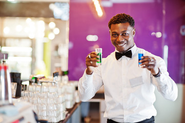 African american bartender at bar holding two coctail shots. Alcoholic beverage preparation.
