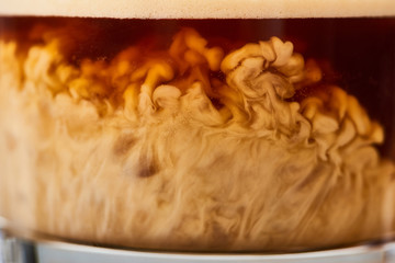 close up view of tasty coffee mixing with milk in glass