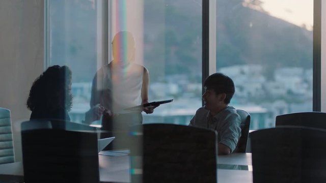 business people working late asian team leader woman meeting with colleagues discussing project manager sharing ideas on tablet computer group of executives brainstorming in office at sunset