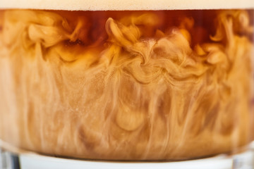 close up view of brown coffee mixing with white milk in glass
