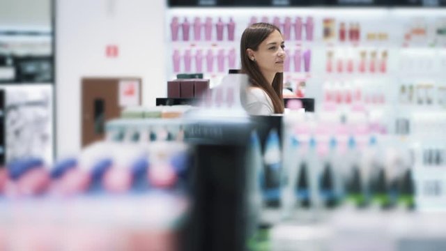 Beautiful girl goes among shelves in cosmetics shop, slow motion, steadicam shot