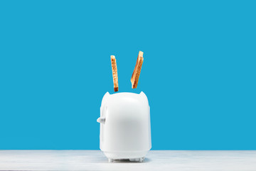 Roasted toast bread popping up of toaster with blue wall