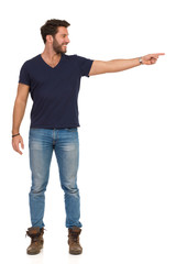 Smiling Handsome Man In Jeans T-Shirt And Boots Is Pointing And Looking Away