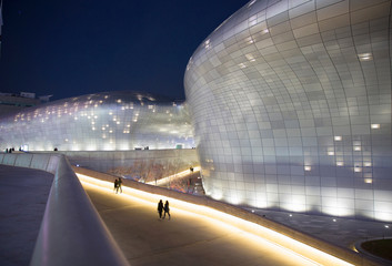 People walking by modern illuminated building at night