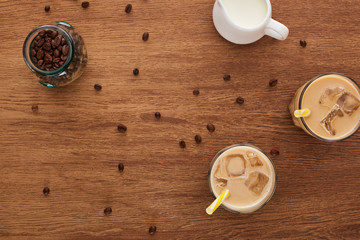 top view of ice coffee in glasses, milk and coffee grains on wooden table