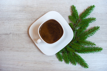Obraz na płótnie Canvas White cup of coffee with fir branches on a light wooden background. Beautiful white cup, stylish toning, place for text. Cup of black tea. Cheerful christmas morning concept. Top view