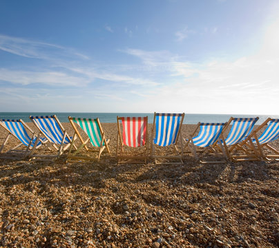 View of deckchairs on pebble beach against cloudy sky