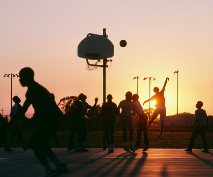Silhouette of group of men playing basketball during sunset