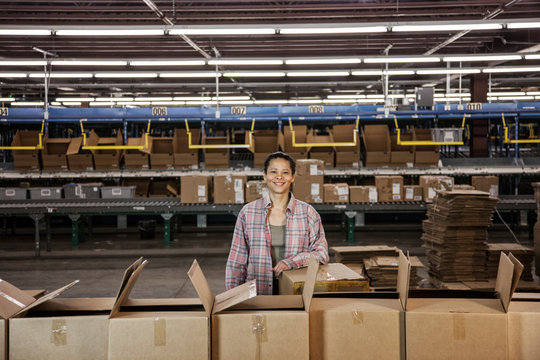 Portrait of smiling woman standing by cardboard boxes in distribution warehouse