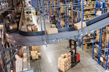 View of conveyor belt, racks and forklift trucks in distribution warehouse