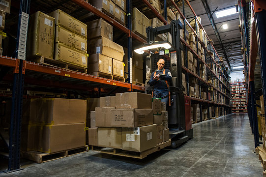 Worker operating stock picker loaded with cardboard boxes in warehouse