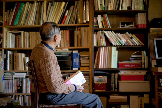 Side view of senior man sitting on chair in front of book shelf