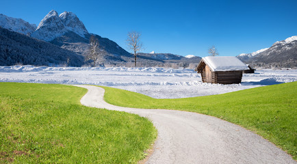 Fotomontage Klimawandel, grüne Wiese mit Kurvenweg und Winterlandschaft im Gebirge mit Hütte