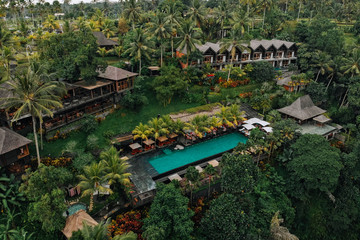 Aerial view of luxury hotel with straw roof villas and pools in tropical jungle and palm trees. Luxurious villa, pavilion in forest, Ubud, Bali