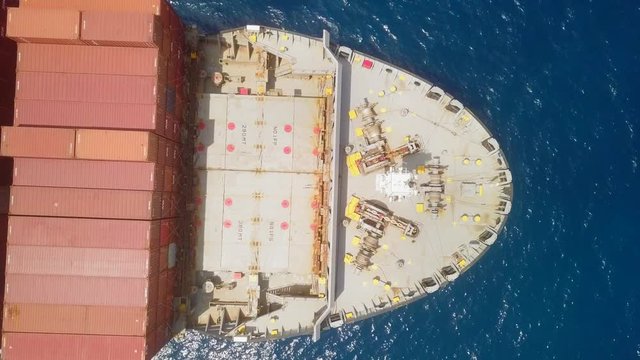 Aerial footage of a large container ship at sea, loaded with various container brands