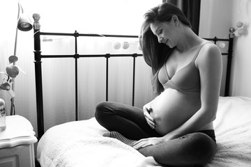 pregnant woman with nacked belly sitting om a bad in the room, haging the belly