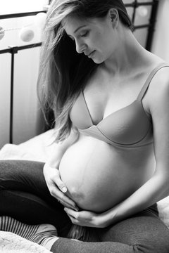 pregnant woman with nacked belly sitting om a bad in the room, haging the belly