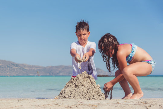 Cute little boy and a girl building a sand castle on a tropical sea shore. Summer vacation with family concept.