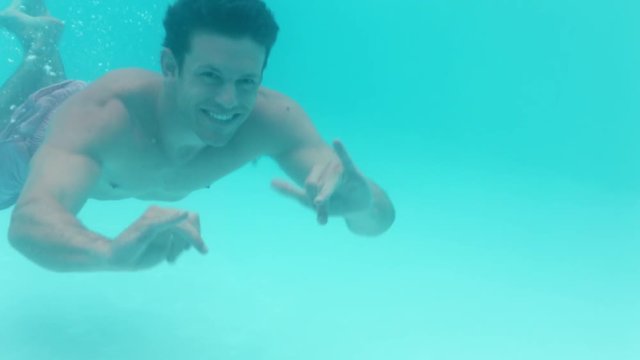 attractive young man swimming underwater in pool waving hand smiling happy floating in crystal clear water having fun swim in summertime 4k