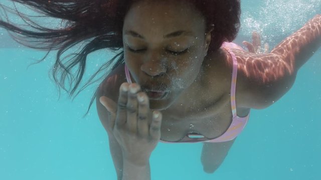 beautiful african american woman swimming underwater in pool smiling blowing kiss floating in blue crystal clear water having fun swim in summertime 4k