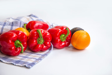 Sweet peppers, oranges and avocado in a tea towel on a white table