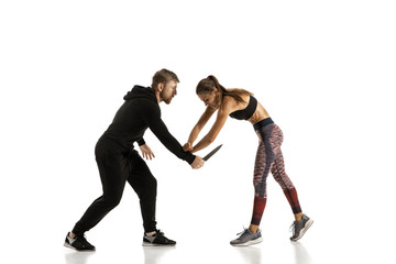 Man in black outfit and athletic caucasian woman fighting on white studio background. Women's...