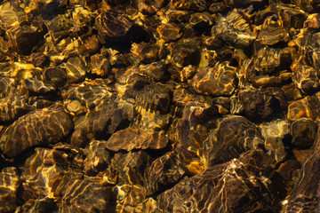 Shiny transparent water. clear water with pebbles and stone on the bottom. shining reflections of sun rays and ripples on the water