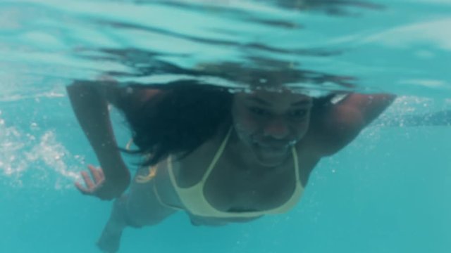 beautiful african american woman swimming underwater in pool smiling floating in blue crystal clear water having fun swim in summertime 4k