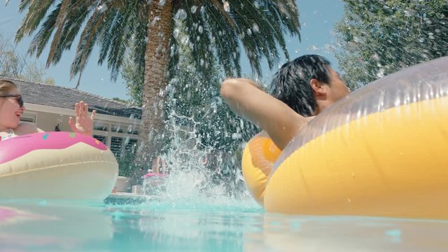 summertime fun friends jumping in swimming pool playfully splashing people on swim tubes celebrating summer vacation on colorful swim floats 4k