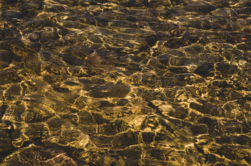 Shiny transparent water. clear water with pebbles and stone on the bottom. shining reflections of sun rays and ripples on the water