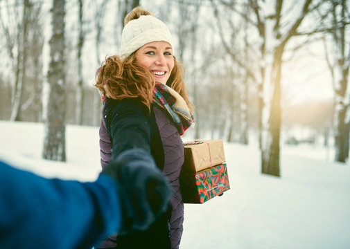 POV image of a diverse couple holding Christmas presents while walking through a winter forest