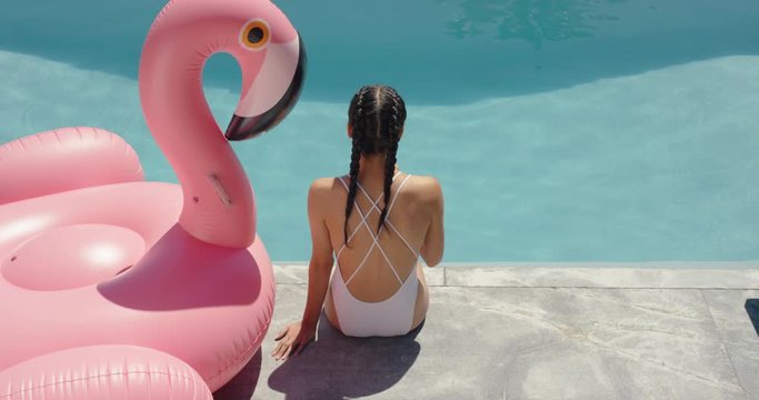 bikini woman sitting by swimming pool with drink enjoying summer day getting sun tan relaxing with pink flamingo swim tube inflatable 4k
