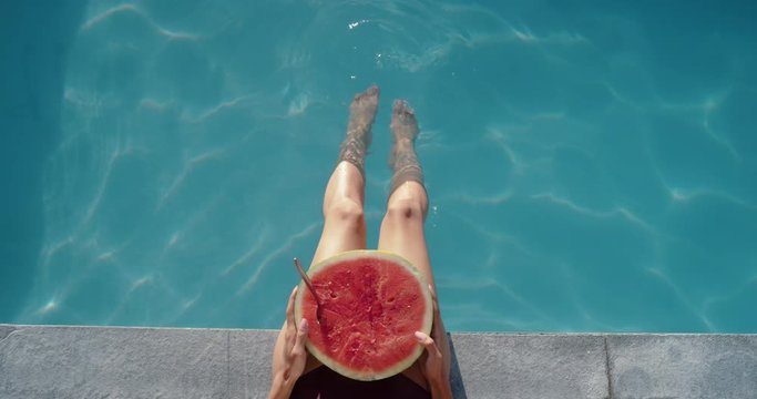 beautiful woman legs in swimming pool with watermelon fruit playfully splashing water with feet enjoying relaxing summer vacation 4k