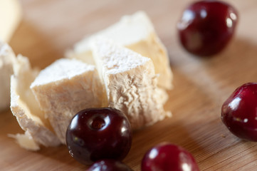 Camembert from goat's milk cut into slices on a wooden board still life with sweet cherry berries close-up
