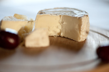Camembert from goat's milk cut into slices on a wooden board still life with sweet cherry berries. With a clear glass lying on the plan is out of focus