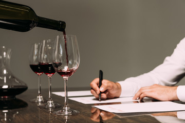 partial view of sommelier writing at table with wine glasses