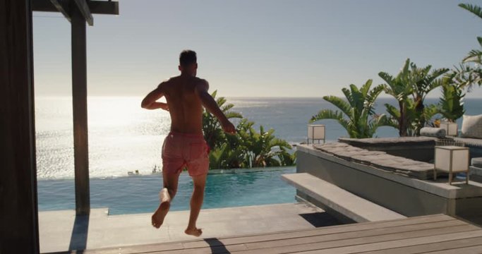 young man running jumping in swimming pool at luxury hotel with beautiful ocean view having fun summer vacation enjoying swim at tropical resort on warm sunny day mediterranean travel 4k