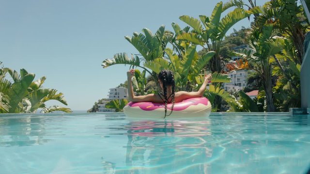 beautiful woman relaxing on pink swim tube floating in swimming pool drinking juice getting sun tan on warm sunny day enjoying summer vacation at luxury hotel resort with view of ocean palm trees 4k