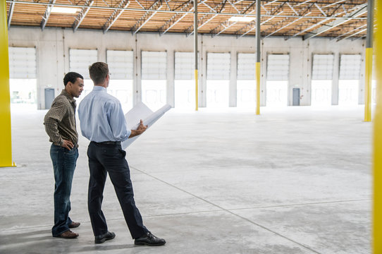 Owner and architect talking over blueprints in warehouse