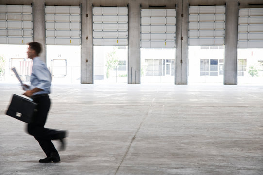Side view of architect with briefcase and blueprint running in warehouse