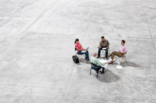 Architects talking over blueprint while sitting in warehouse