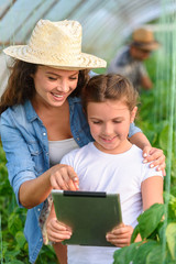 Mother and daughter growing organic vegetables at greenhouse. Small family business.