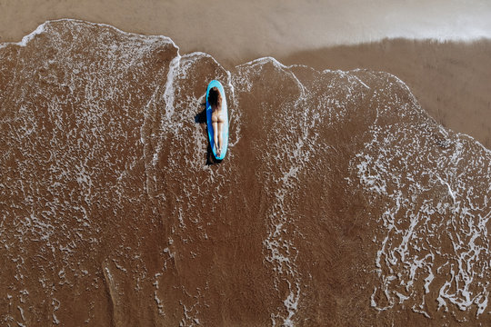 Aerial drone view of a woman in bikini takes a sunbath on a surfboard over the tropical, turquoise waters on ocean beach of Bali Indonesia. Tropical background and travel sport concept.