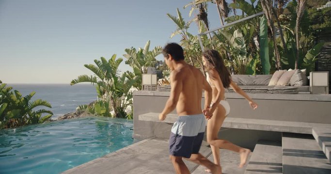 fun couple jumping in swimming pool splashing having fun romantic summer vacation on honeymoon at luxury hotel resort with beautiful ocean view at sunset 4k
