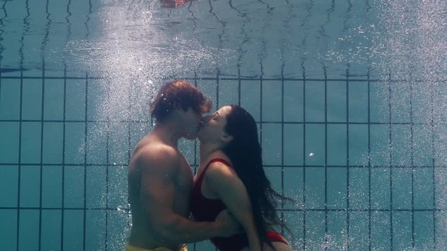 underwater couple kissing in swimming pool young people in love enjoying romantic kiss passionate lovers submerged in water floating with bubbles in playful intimacy 